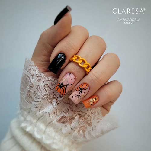 Black and orange autumn nails featuring orange pumpkins on two nude accent nails, capturing the essence of fall.