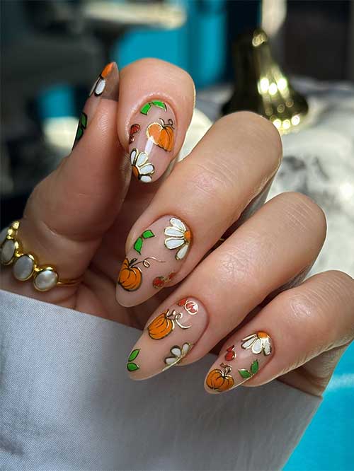 Stylish pumpkin nails showcasing orange pumpkins, white floral accents, and green leaves on a nude background.