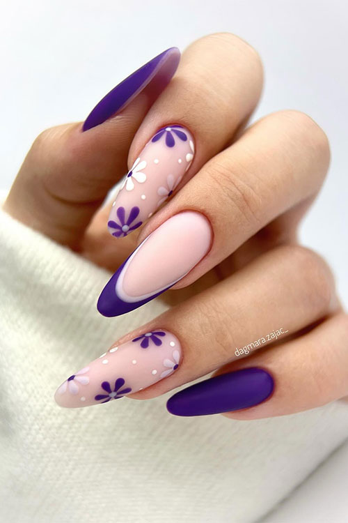 Long almond-shaped matte dark purple nails with two accent nude nails adorned with flowers and dots