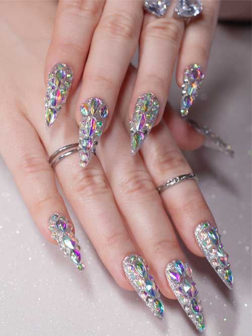 Long almond-shaped silver nails adorned with colorful 3D rhinestones, showcasing a dazzling bling effect.