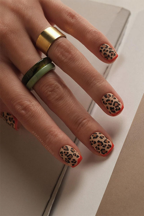 Short brown and black leopard print nails over matte nude base color with minimalist orange French tips