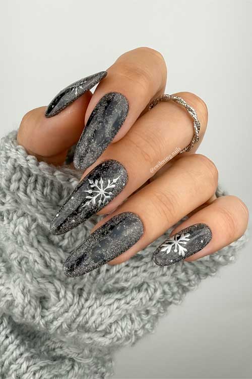 Elegant long almond-shaped black nails design with silver glitter, complemented by two accent nails showcasing snowflakes