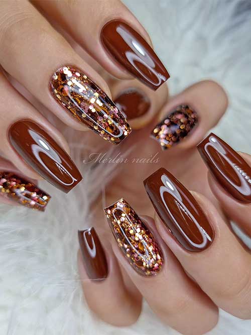 Glossy coffin brown fall nails with two glitter accent nails create a striking and bold manicure choice.