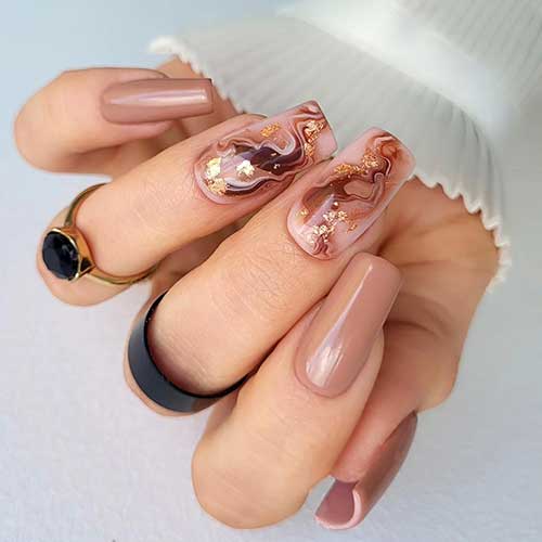 Light brown nails with two accent marble designs on a nude base, creating an elegant and understated manicure.