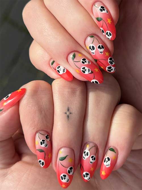 Long almond-shaped ombre orange nails adorned with cherry skull designs, perfect for a festive Halloween look.