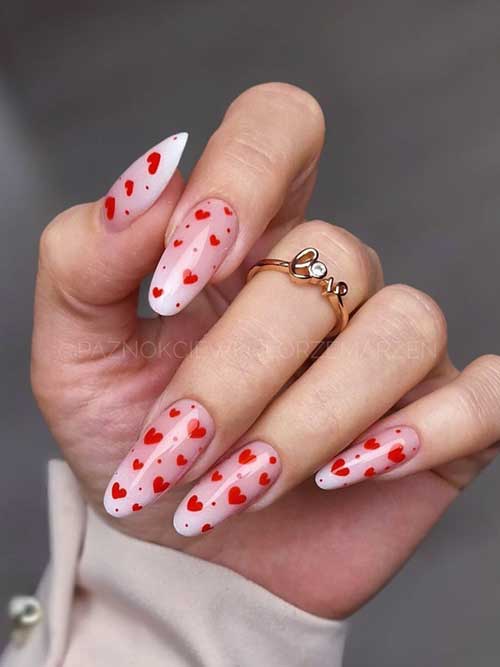 Long almond-shaped baby boomer Valentine nails decorated with tiny red hearts for a festive Valentine's Day look.