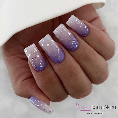 Ombre nails transitioning from purple to milky white, adorned with delicate silver glitter accents.