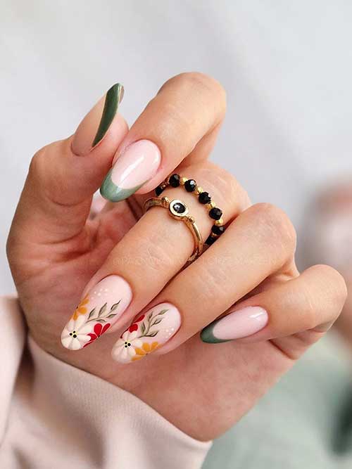 Almond-shaped green French tip nails with two nude accent nails featuring floral and leaf designs for a stylish look.