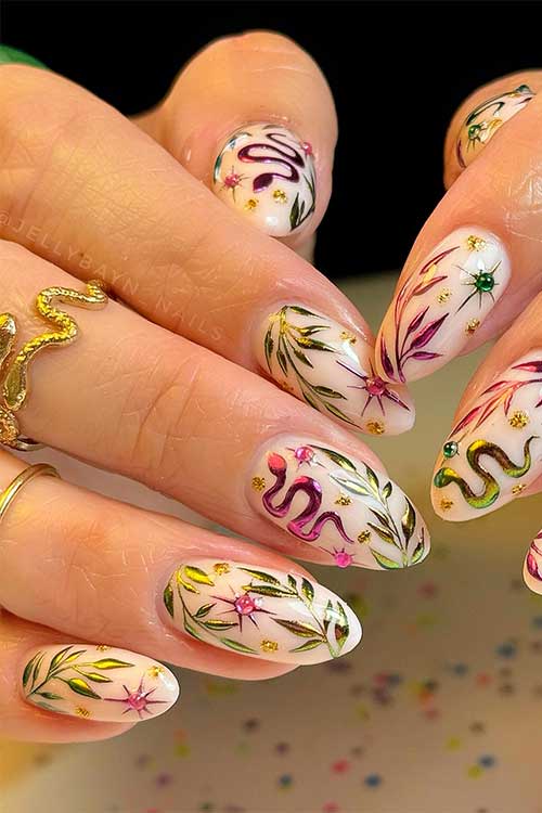 Creative autumn nails with a milky white base, featuring chrome pink and green snakes, gold leaves, and star nail art with rhinestones.