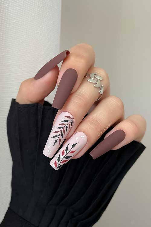 Long matte brown coffin nails with two nude pink accent nails featuring leaf art and silver foil embellishments.