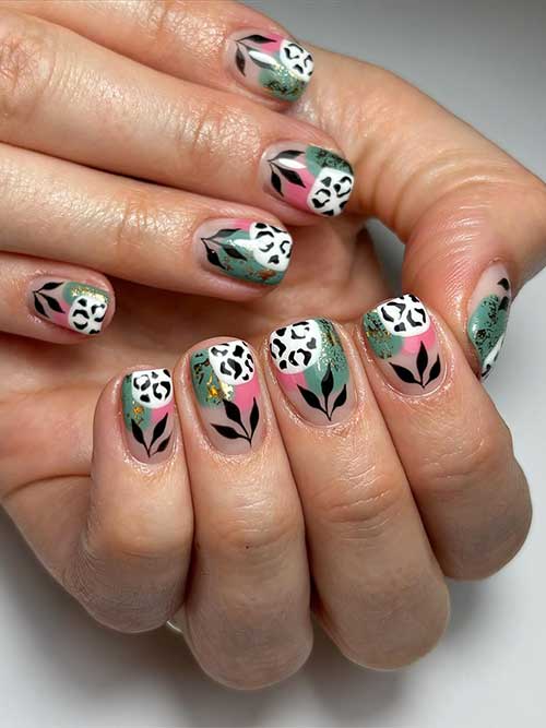 Short abstract nails in pink, green, and white over a nude base, embellished with black leopard prints and leaf art at the cuticles.