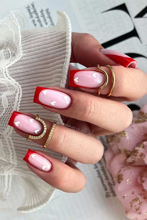 Square-shaped Valentine red French tip nails on a nude pink base, adorned with charming white heart designs.