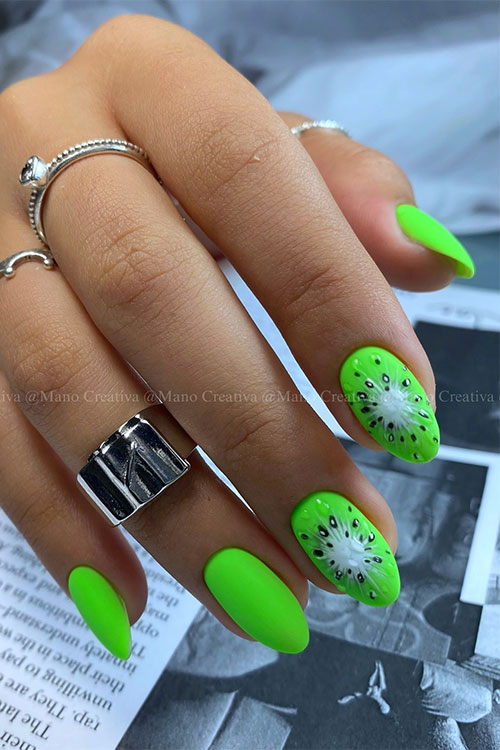 Medium almond-shaped matte neon green nails with two accents adorned with kiwi fruit nail art