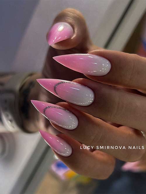 Long stiletto-shaped Barbie pink and white ombre nails with two accent nails adorned with glitter negative space French tips