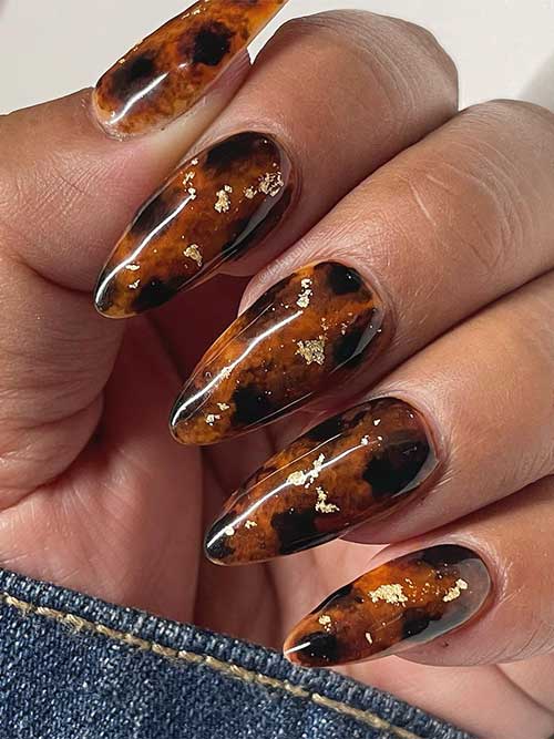 Elegant almond-shaped tortoise nails for fall, embellished with shimmering gold foil pieces for a chic look.