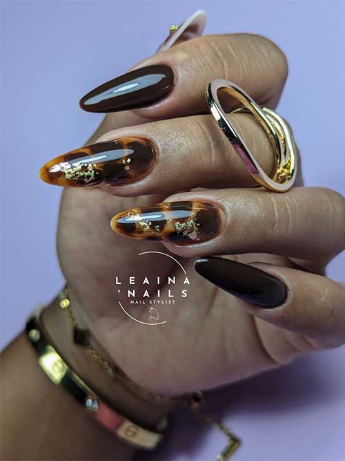 Glossy long almond-shaped brown and tortoise shell nails adorned with decorative foil pieces for an elegant look.