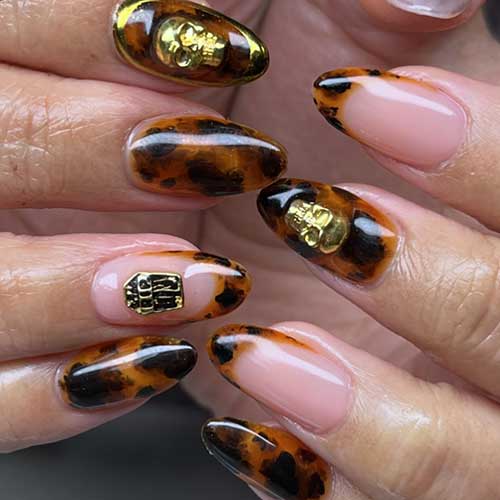 Halloween-themed tortoise nails in almond shape, adorned with gold rhinestones featuring skulls and coffins.