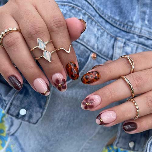 Short brown nails featuring tortoise and floral designs, embellished with gold rhinestones for an elegant touch.