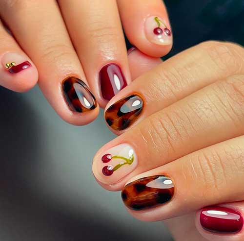 Short tortoise shell nails featuring burgundy, French tips, and accent nails adorned with cherry designs.