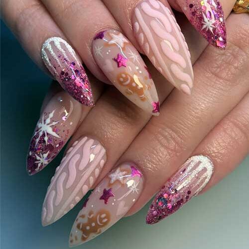 Cute almond-shaped Christmas nails with pink glitter tips, icicle art, and gingerbread, star, and heart designs on nude base.