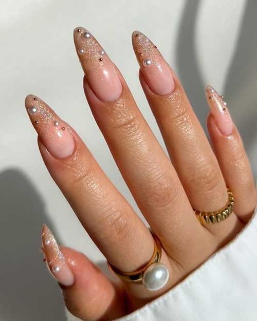 Long almond-shaped ombre New Year nails feature nude to gold glitter ombre style and are decorated with white pearls.