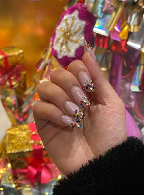 Long nude nails adorned with vibrant rhinestones at the tips, showcasing a stylish and eye-catching manicure.