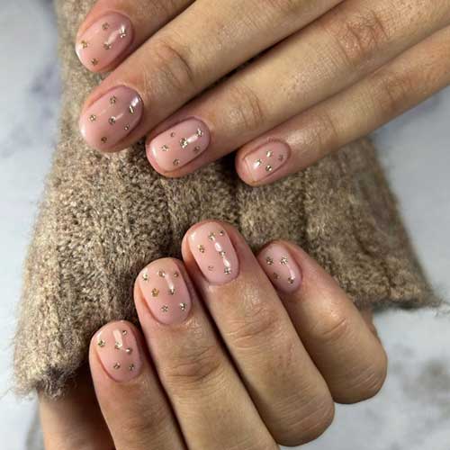 Simple new years nails feature short nude nails with gold glitter dots.