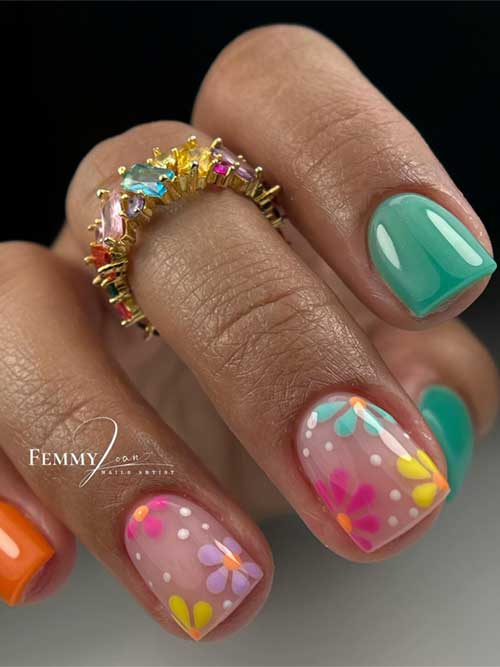 Bright orange and teal nails with floral patterns in pink, yellow, and blue, accented by a gold ring with colorful gemstones.