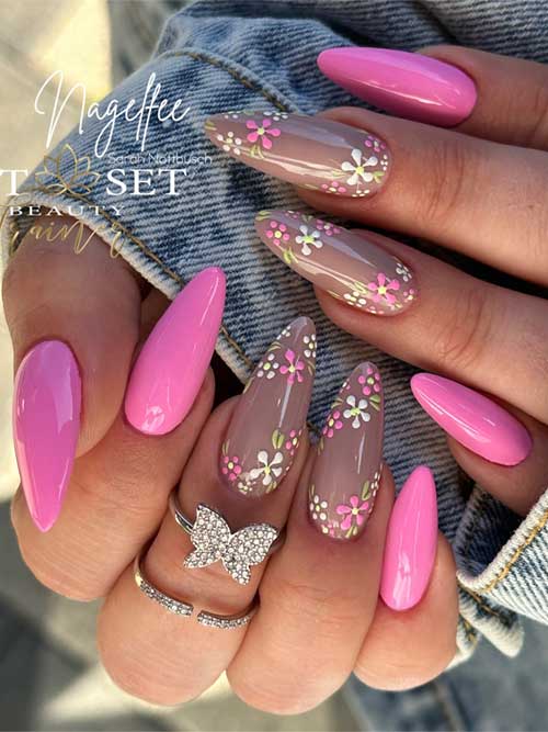 Bright pink and nude almond-shaped nails with floral designs, complemented by a sparkling butterfly ring for a fresh spring look.