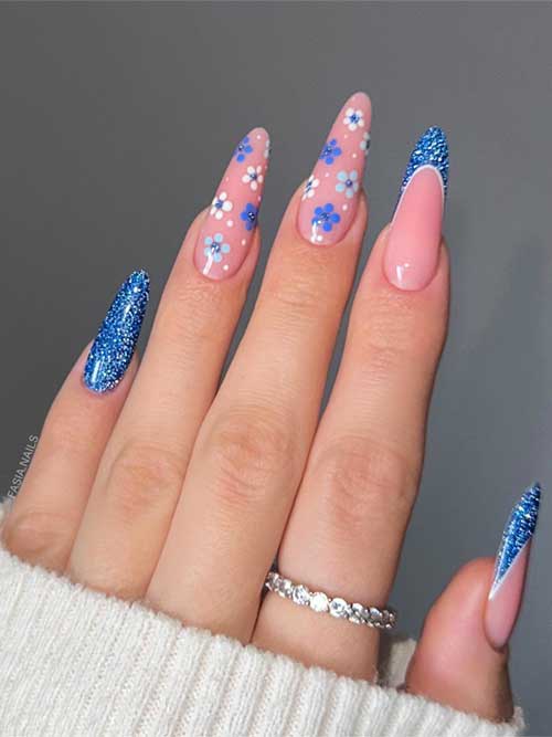 Long almond-shaped floral nails with blue glitter, pink bases, and blue tips capture seasonal beauty and glamour.