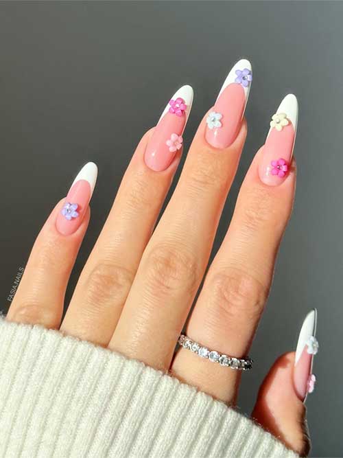 Long almond-shaped nails with soft pink bases, white tips, and colorful 3D flower embellishments in purple, pink, and white.