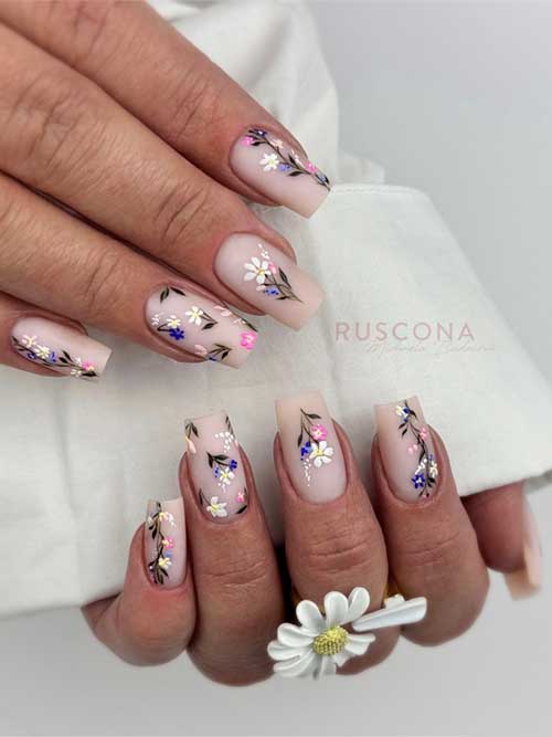 Nude nails adorned with delicate floral designs in white, pink, blue, and yellow, embodying a fresh springtime vibe.