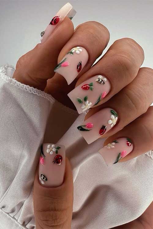 Soft nude nails with floral designs and ladybugs, featuring white flowers, pink tulips, and red ladybugs for a spring vibe.